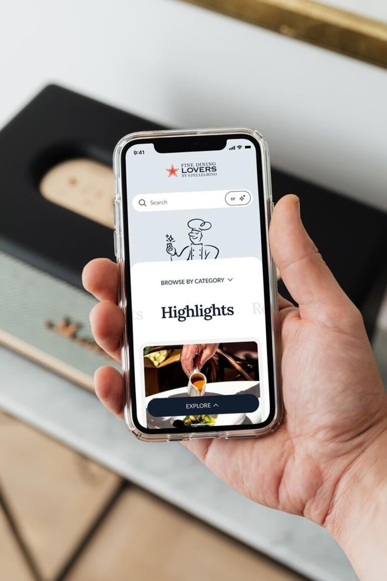 Una mano sostiene un teléfono que muestra una página de Fine Dining Lovers